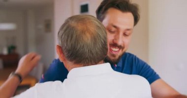 Gülümseyen genç bir adam yaşlı babasına evde sarılır.