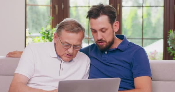 Bir baba ve oğlu evdeki bir kanepede dizüstü bilgisayar kullanıyor. — Stok video
