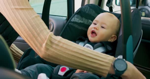 車の中のベビーカーシートに座っている赤ちゃんの男の子を閉じますドアが開き、彼の母親の手は安全ベルトをunfastensし、慎重に車から赤ちゃんを取るスローモーション — ストック動画