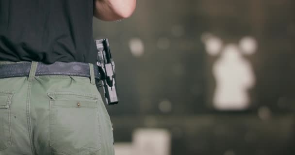 Vista trasera primer plano de un hombre que devuelve una pistola a su funda después de disparar un tiro a un campo de tiro interior — Vídeo de stock