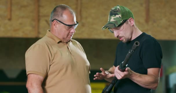 De stagiair zet een beschermende bril en oortelefoon op voordat hij onder toezicht van een instructeur een schot afvuurt op een gesloten schietbaan. Een man leert schieten met een jachtgeweer. — Stockvideo