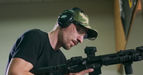 A man loads a magazine clip onto a rifle and fires a round at an indoor firing range — Stock Video