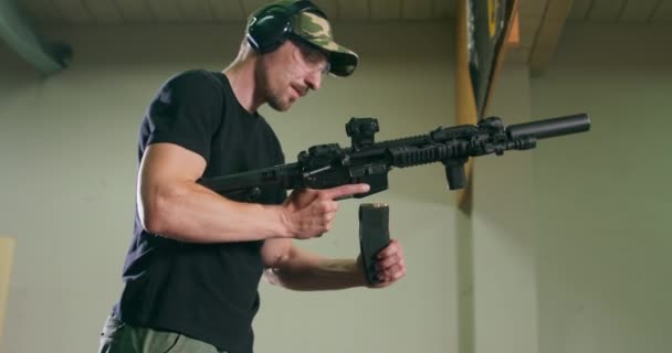Een man met een bril en gehoorbescherming laadt een lang pistool uit door de magazijnclip te verwijderen en te controleren op kogels in de kamer op een indoor schietbaan. — Stockvideo