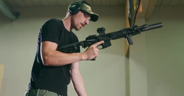 Muž s brýlemi a chráničem uší vyloží dlouhou zbraň tak, že vyndá zásobník a zkontroluje náboje v komoře na střelnici. — Stock video