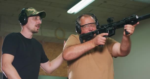 Человек учится стрелять из винтовки на стрельбище инструктор показывает ученику правильное положение стрельбы — стоковое видео