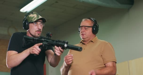 Человек учится стрелять из винтовки на стрельбище инструктор показывает ученику правильное положение стрельбы — стоковое видео