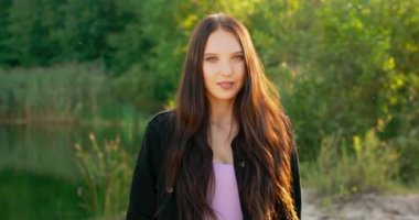 Gölün yakınındaki bir ormanda uzun siyah saçlı, gülümseyen genç bir kadının portresi.