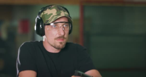 Een schietinstructeur met een beschermende bril en een koptelefoon richt zich op een doelwit en vuurt een schot af op een indoor oefenbereik — Stockvideo