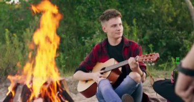 Nehir kenarında piknik yaparken arkadaşlarıyla konuşan genç bir çocuğun görüntüsü. Gün batımında boş vakit geçiriyor. Genç kız gitar çalacak.