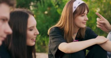 Nehir kıyısında piknik yaparken arkadaşlarına gülümseyen güzel bir genç kızın parlak gün batımında gülerek boş vakit geçirmesini yakından izleriz.