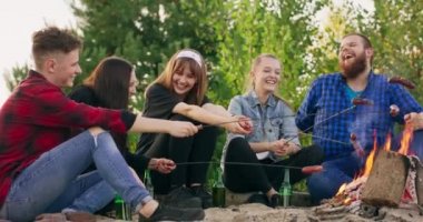 Çok kültürlü bir arkadaş grubu plajda parti yapıyor yaz tatilinde kutlama yapan gençler sosis pişiriyor, bira içiyor, konuşuyor ve eğleniyorlar.