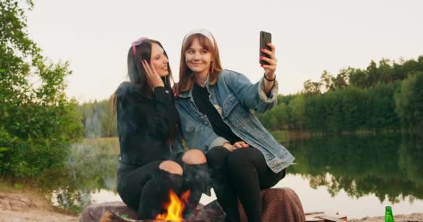 De jonge meisjes zitten bij het vuur en maken een selfie foto — Stockvideo