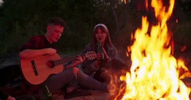 Hippi adam akustik gitar çalıyor ve arkadaşlarıyla şarkı söylüyor. Gece kampındaki büyük şenlik ateşinde gezginler göl kenarında kamp yapan bir grup insan.