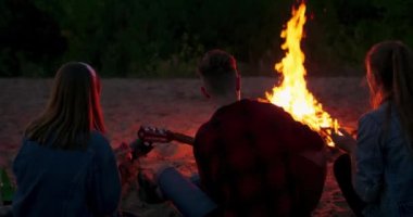 Hippi adam akustik gitar çalıyor ve arkadaşlarıyla şarkı söylüyor. Gece kampındaki büyük şenlik ateşinde gezginler göl kenarında kamp yapan bir grup insan.