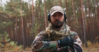 Orta yaşlı, sakallı bir askerin portresi Woodland askeri üniforması ve kafasında kulaklıkla göğsünde kollarını bağlayan bir asker.