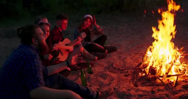 En grupp vänner som njuter av en gitarrföreställning vid lägerelden — Stockvideo