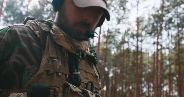 Porträtt av en skäggig fokuserad seriös medelålders soldat i en militäruniform från skogslandet och en mössa med hörlurar på huvudet som väntar på att handling ska börja i skogen — Stockvideo