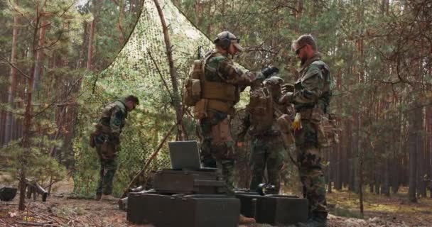 El comandante comprueba el equipo del uniforme y la corrección de ponerse el chaleco táctico de los soldados antes de ir a la acción Un bosque de pinos caliente es el fondo — Vídeos de Stock