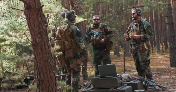 Un grupo de soldados en uniforme militar se prepara para entrar en acción en una base forestal temporal. El comandante comunica los arreglos y el plan de acción a sus soldados. — Vídeos de Stock