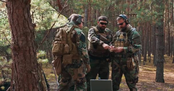 En grupp soldater i militäruniform gör sig redo för strid i en tillfällig skogsbas Befälhavaren kommunicerar arrangemangen och handlingsplanen till sina soldater. — Stockvideo