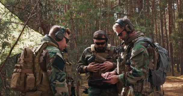 Un grupo de soldados barbudos de mediana edad en uniformes y chalecos tácticos discute el plan de acción y se prepara para la acción en una base forestal temporal. — Vídeos de Stock