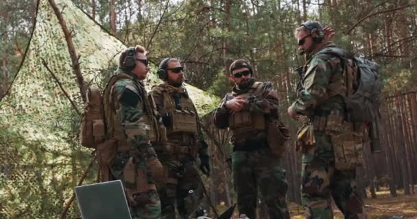 Un groupe de soldats barbus d'âge moyen en uniforme et vestons tactiques discute du plan d'action et se prépare à l'action dans une base forestière temporaire Le commandant donne des instructions aux soldats — Video