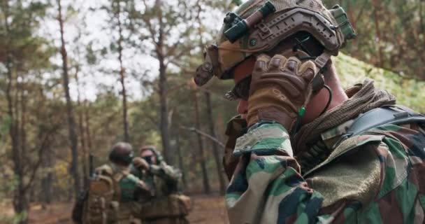 Soldat en uniforme militaire portant un casque tactique dans une base forestière temporaire — Video