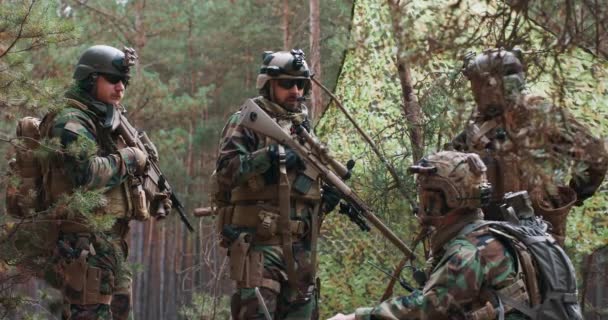 Vousatí vojáci v lesních uniformách s helmami na hlavách a s puškami v rukou se vrátili z průzkumu a hlásili se veliteli čety na dočasné lesní základně. — Stock video
