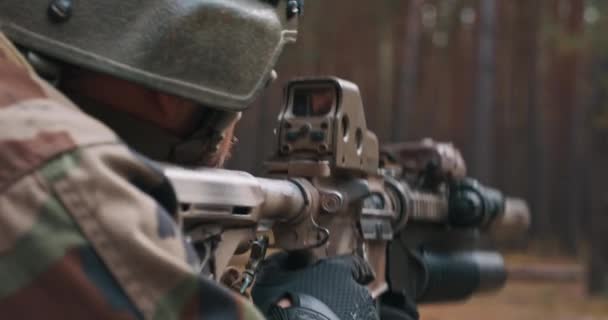Żołnierz w specjalnym mundurze wojskowym z hełmem na głowie i karabinem snajperskim w lesie celującym przez lunetę. — Wideo stockowe