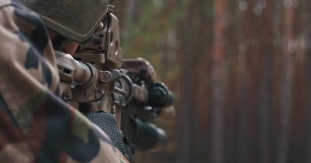 Un soldat en uniforme militaire spécial avec un casque sur la tête et un fusil de sniper dans la forêt visant à travers une lunette — Video