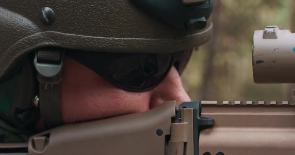 Close up de soldado em um uniforme militar especial com um capacete na cabeça e com um rifle sniper na floresta visando através de um escopo — Vídeo de Stock