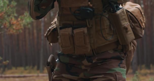 Een bebaarde soldaat in een tactisch militair uniform, met een helm op zijn hoofd en een sluipschuttersgeweer in het bos, gericht op de vijand door een telescoop. — Stockvideo