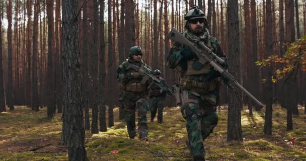 Escuadrón de cuatro soldados totalmente equipados en camuflaje en una misión militar de reconocimiento apuntando a rifles que se mueven en formación a través de imágenes densas del bosque al mediodía — Vídeos de Stock
