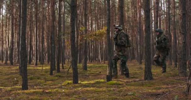 Fullt utrustade soldater bär kamouflage enhetlig attack fiendens gevär i skottläge militär operation i aktion trupp kör i Bildning genom tät skog vid middagstid — Stockvideo