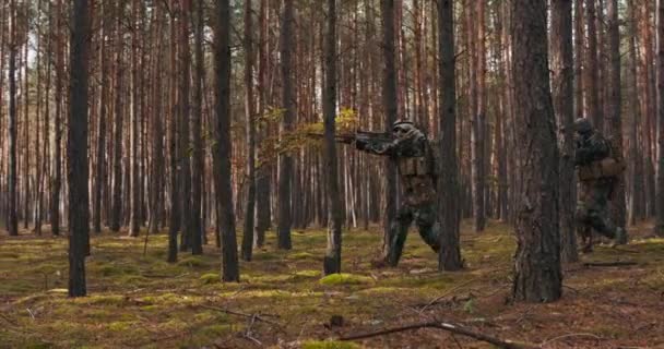 迷彩服を着た完全装備兵士が真昼の鬱蒼とした森の中を駆け抜けるアクション分隊での射撃位置で敵ライフルを攻撃 — ストック動画