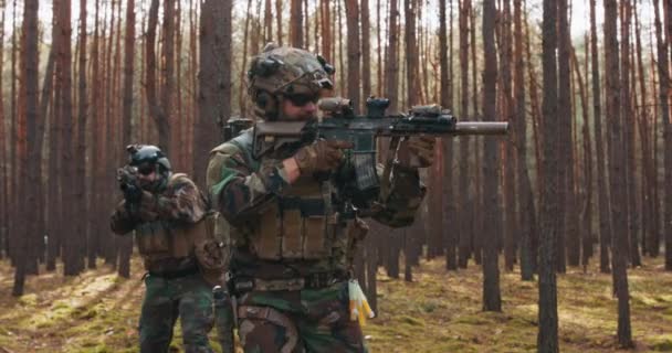 Escuadrón de cuatro soldados totalmente equipados en camuflaje en una misión militar de reconocimiento apuntando a rifles que se mueven en formación a través del denso bosque de pinos — Vídeos de Stock