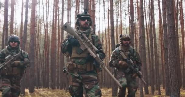 Cuatro soldados de mediana edad totalmente equipados con uniformes de camuflaje forman una línea lista para disparar apuntando con sus rifles Una operación militar en acción una unidad de pie en un denso bosque — Vídeos de Stock