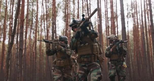 Escuadrón de cuatro soldados totalmente equipados en camuflaje en una misión militar de reconocimiento apuntando a rifles que se mueven en formación a través del denso bosque — Vídeos de Stock