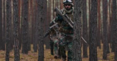 Tam teçhizatlı orta yaşlı dört asker silahlarını ateşlemeye hazır bir sıra oluşturdular. Yoğun bir ormanda ayakta duran bir askeri operasyon.