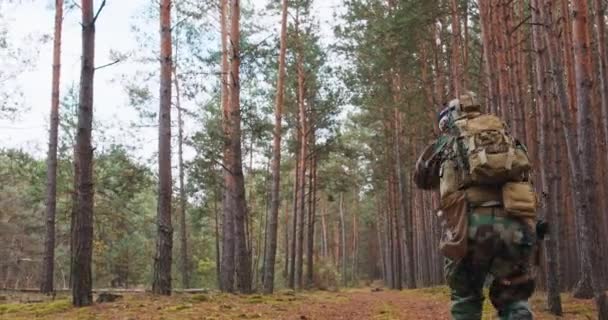 Πλήρως εξοπλισμένοι στρατιώτες με στολή καμουφλάζ που επιτίθενται σε εχθρικά τουφέκια στη θέση βολής Στρατιωτική επιχείρηση σε ομάδα δράσης που παραμένει σε σχηματισμό μέσω πυκνού δάσους το μεσημέρι — Αρχείο Βίντεο