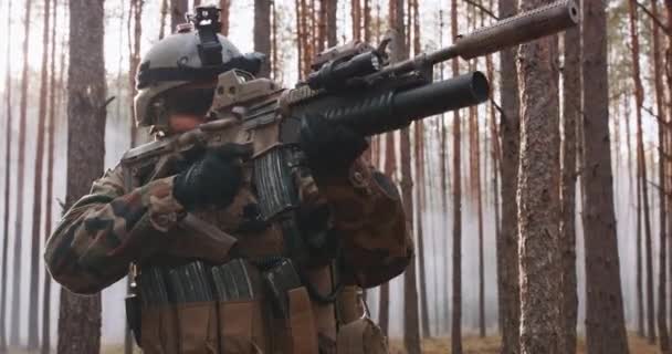Солдат у спеціальній військовій формі з шоломом на голові і снайперською гвинтівкою в лісі, спрямованою через приціл — стокове відео