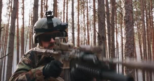 Um soldado com um uniforme militar especial com um capacete na cabeça e um rifle sniper na floresta apontando através de um escopo — Vídeo de Stock