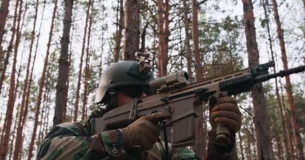 머리에 헬멧을 쓴 특수 군복을 입고 숲 속에서 저격수 소총을 든 한 군인 이 프레임에 스코프 선셋의 발광을 목표로 하고 있다 — 비디오