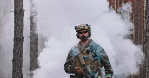 松林の真ん中に煙のパフから出てくるカモフラージュの制服を着た完全装備の兵士 — ストック動画