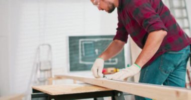 Bir marangoz atölyesindeki tahtayı ölçerken elinde cetvel ve kalem tutan çalışkan bir marangozun yakın çekimi. Sakallı bir DIY meraklısı odunları ölçer.
