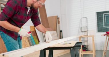 Bir marangoz atölyesindeki tahtayı ölçerken elinde cetvel ve kalem tutan çalışkan bir marangozun yakın çekimi sakallı bir DIY meraklısı odunu ölçer.