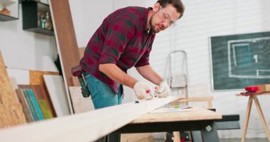 Bir marangoz atölyesindeki tahtayı ölçerken elinde cetvel ve kalem tutan çalışkan bir marangozun portresi. Sakallı bir DIY meraklısı tahtayı ölçüyor. Çilingir masası ve aletler var.