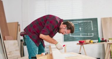 Bir marangoz atölyesindeki tahtayı ölçerken elinde cetvel ve kalem tutan çalışkan bir marangozun portresi. Sakallı bir DIY meraklısı tahtayı ölçüyor. Çilingir masası ve aletler var.