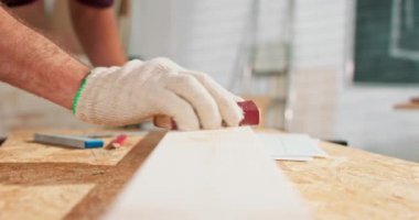 Sakallı bir tamirci marangoz atölyesinde mobilya yapmak için odun zımparalıyor. Marangoz tahtayı zımparaladıktan sonra cipsleri uçuruyor.