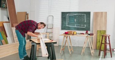 Bir marangoz atölyesindeki tahtayı ölçerken elinde cetvel ve kalem tutan çalışkan bir marangozun yakın çekimi. Sakallı bir DIY meraklısı odunları ölçer. Çilingir masası var.